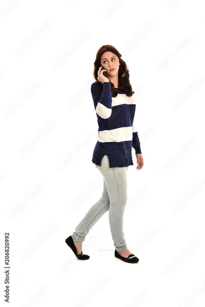 full length portrait of girl wearing striped blue and white jumper and jeans, holding a phone. standing pose on white studio background full length portrait of girl wearing striped blue and white jumper and jeans, holding a phone. standing pose on white studio background