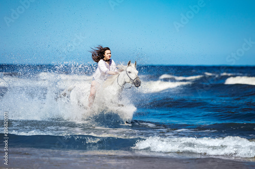 Girl on a white horse storming through the water