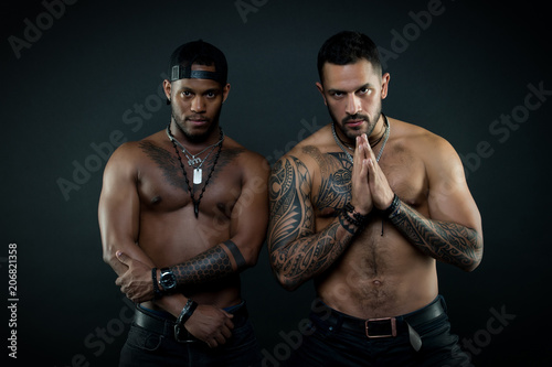 Athletes on confident faces with nude muscular chests.Machos with muscular tattooed torsos look attractive, dark background. Sexy body concept. Guys sportsmen with sexy muscular torsos