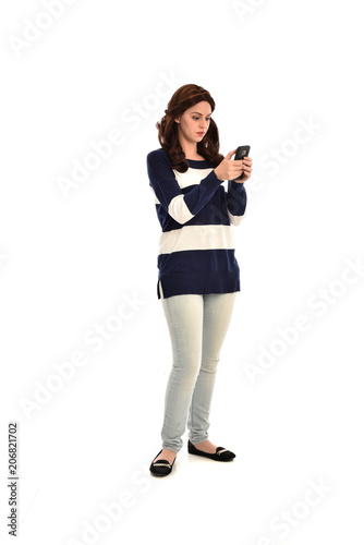 full length portrait of girl wearing striped blue and white jumper and jeans, holding a phone. standing pose on white studio background © faestock