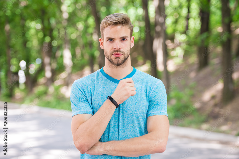 Man athlete on strict face posing with sportive equipment, nature background. Athlete with bristle with fitness tracker or pedometer. Sport gadget concept. Sportsman training with pedometer gadget Man athlete on strict face posing with sportive equipment, nature background. Athlete with bristle with fitness tracker or pedometer. Sport gadget concept. Sportsman training with pedometer gadget