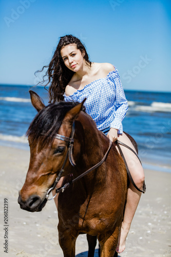 Young attractive girl sitting on a bay horse by the sea