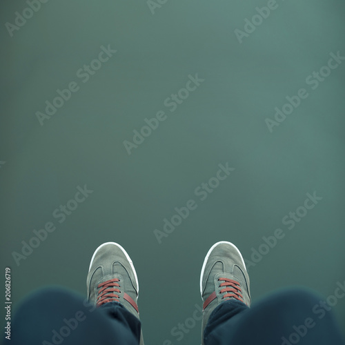 Minimal picture some legs with green sneakers over a green abyss, background, water, environment.