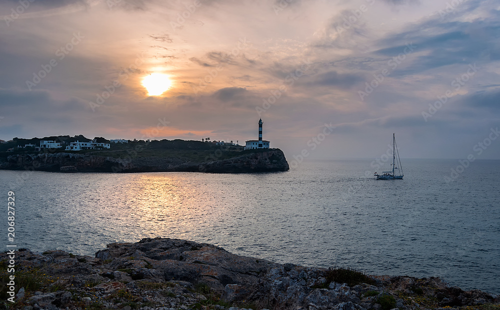 Lighthouse and boat at sunrise in Porto Colom, Mallorca, Balearic Islands, Spain.