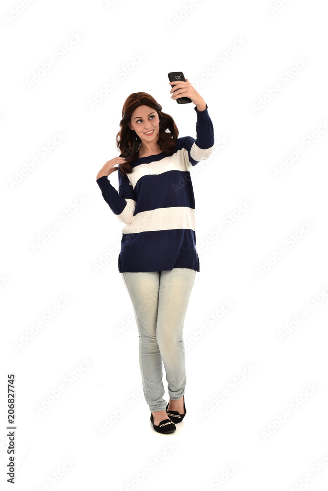 full length portrait of girl wearing striped blue and white jumper and jeans, holding a phone. standing pose on white studio background full length portrait of girl wearing striped blue and white jumper and jeans, holding a phone. standing pose on white studio background