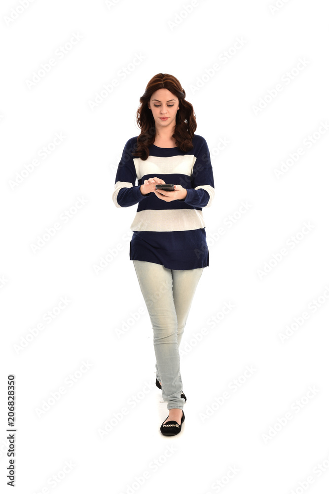 full length portrait of girl wearing striped blue and white jumper and jeans, holding a phone. standing pose on white studio background full length portrait of girl wearing striped blue and white jumper and jeans, holding a phone. standing pose on white studio background
