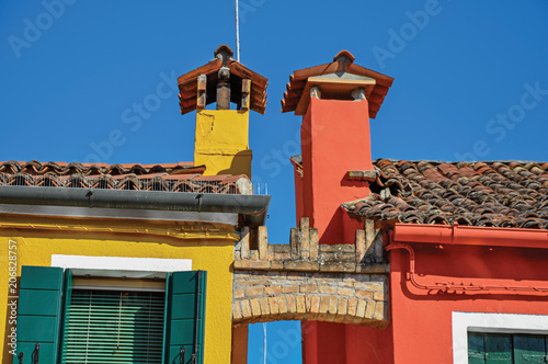 Close-up of chimneys and arch between colorful terraced houses on sunny day in Burano, a gracious little town full of canals, near Venice. Located in the Veneto region, northern Italy