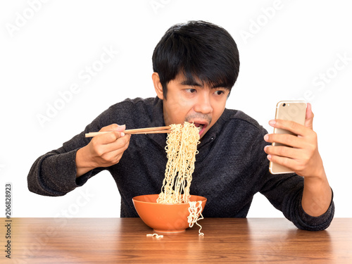 Man eating chinese noodle monstrously whilst looking and using smartphone isolate on white background with clipping path. Concept of smartphone addiction, phubbing or social network issues photo