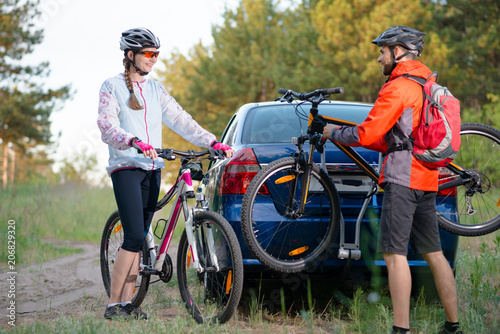 Young Couple Unmounting Mountain Bikes from Bike Rack on the Car. Adventure and Family Travel Concept.