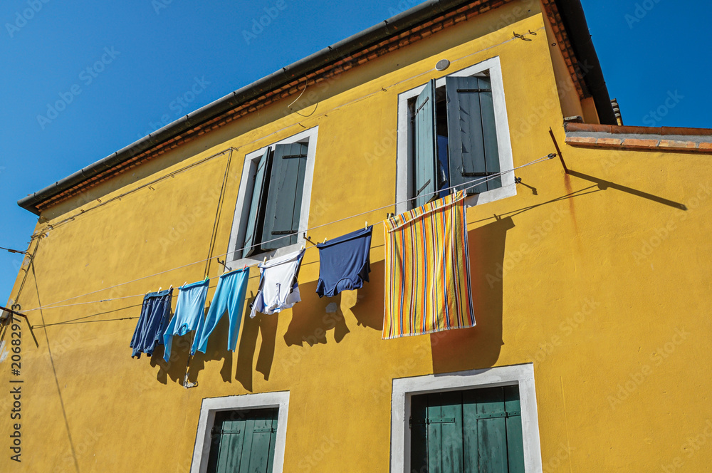 Close-up of windows on colorful walls and clothes hanging on sunny day in Burano, a gracious little town full of canals, near Venice. Located in the Veneto region, northern Italy