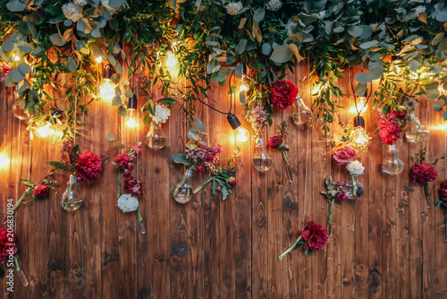 Fototapeta Naklejka Na Ścianę i Meble -  Rustic wedding photo zone. Hand made wedding decorations includes Photo Booth  red flowers. Garlands and light bulbs