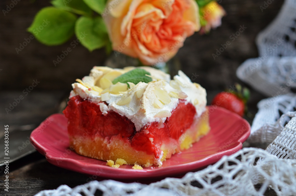 Piece of cake with strawberries and meringue on a wooden background