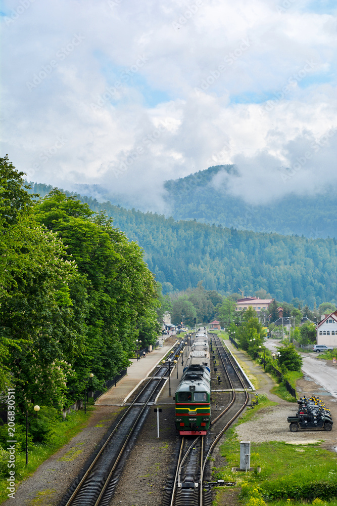 Fototapeta premium Train at the station on the background of the Carpathians. Passenger train in the Carpathians Mountains village. Ukraine