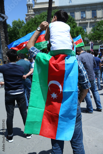 The Azerbaijani flag is on the background of the city . Action . Azerbaijan flag in Baku, Azerbaijan. Put the boy on his shoulder. A flag hanging from his shoulder.