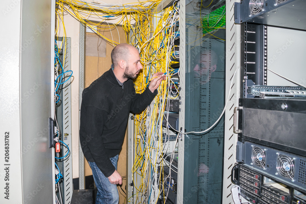 The engineer connects the optical wire to the central router. The system  administrator works in the server room of the data center. The network  engineer is next to the server racks Stock-Foto