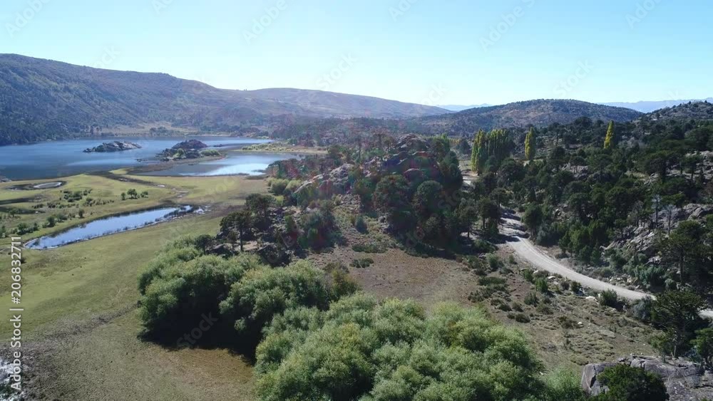 Aerial drone scene of Pulmari lake with rock island, trees,araucarias, steppe, a dirt road and blue sky. Camera moving forwards. Aerial drone scene of Pulmari lake with rock island, trees,araucarias, steppe, a dirt road and blue sky. Camera moving forwards.