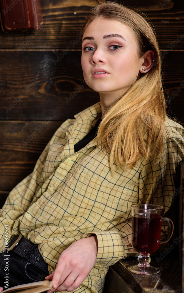 Girl student relaxing with glass of mulled wine, close up. Lady on dreamy face in plaid clothes looks casual. Girl in casual outfit sits in wooden vintage interior. Relaxation concept Girl student relaxing with glass of mulled wine, close up. Lady on dreamy face in plaid clothes looks casual. Girl in casual outfit sits in wooden vintage interior. Relaxation concept