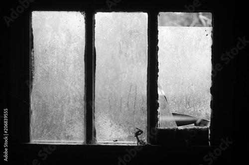 Frosty broken window in a dark derelict building with natural light through dirty panes and cracks