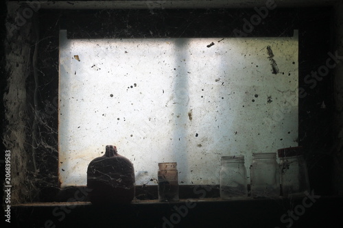 Interior view of frosty window in derelict building. Glass bottles on windowsill among cobwebs in dark room
