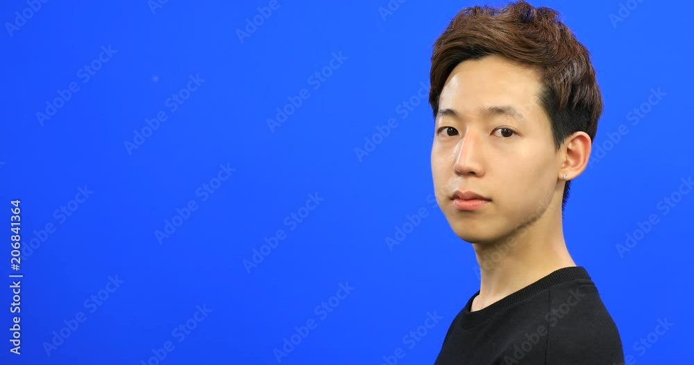 Asian young man turning to camera and making victory sign with his fingers on blue screen Asian young man turning to camera and making victory sign with his fingers on blue screen