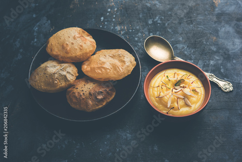 Shrikhand with fried Puri / Poori served in a bowl and plate over moody background. Selective focus photo