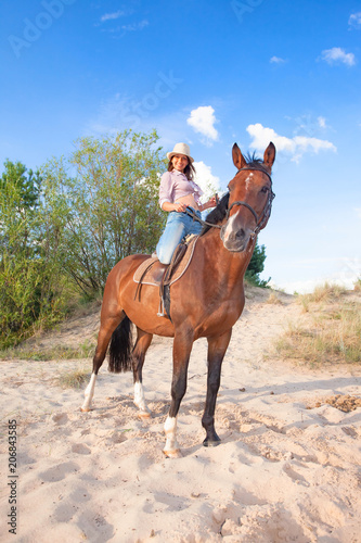 Young beautiful cowgirl with a horse in the dunes.