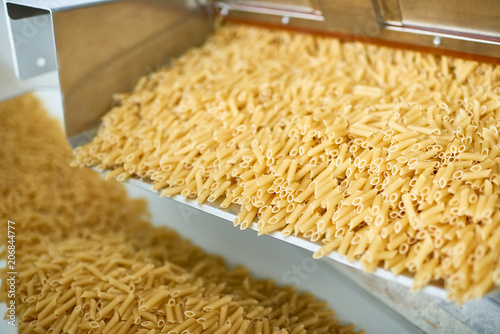 Close up shot of dry macaroni spilling from machine unit on modern food production factory, copy space photo