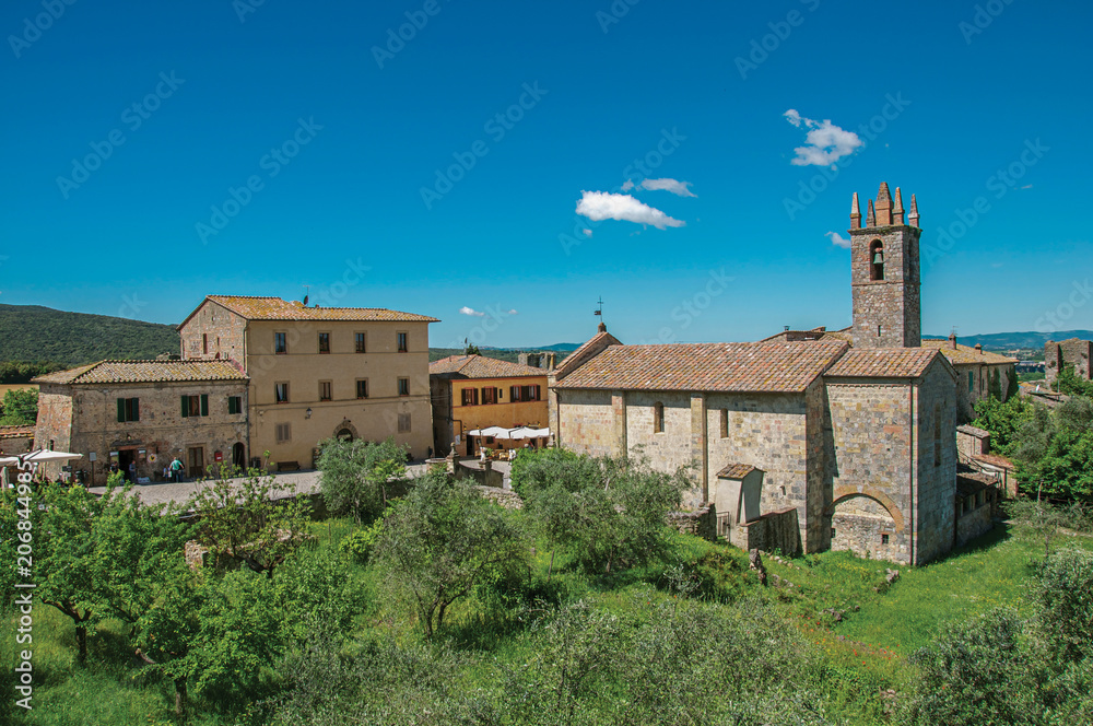 Overview of church and bell tower with trees around in the hamlet of Monteriggioni. A medieval fortress, surrounded by stone walls, at the top of a hill, near Siena. Located in the Tuscany region 