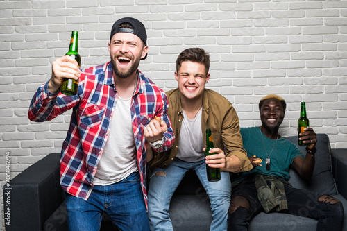 Yes. Winners. Goal. Cheerful young men are watching match on couch at home and drink beer, eat pizza. They are fans of sports games as football, basketball, hockey, baseball photo