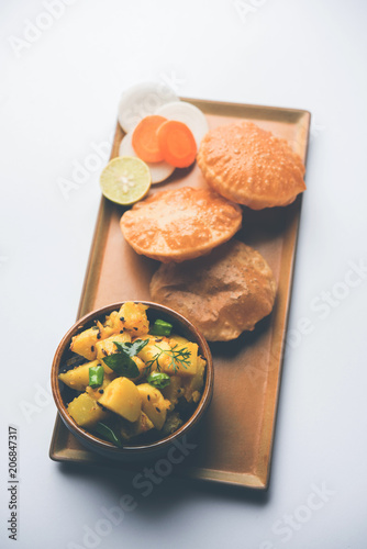 Chatpate Masala Aloo Sabzi fry OR Bombay potatoes served with fried puri or Indian bread made up of wheat in a plate, selective focus photo