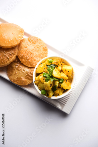 Chatpate Masala Aloo Sabzi fry OR Bombay potatoes served with fried puri or Indian bread made up of wheat in a plate, selective focus photo