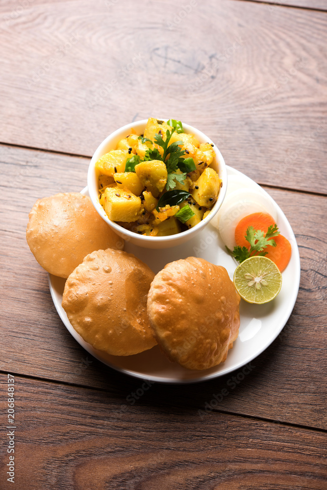 Chatpate Masala Aloo Sabzi fry OR Bombay potatoes served with fried puri or Indian bread made up of wheat in a plate, selective focus Chatpate Masala Aloo Sabzi fry OR Bombay potatoes served with fried puri or Indian bread made up of wheat in a plate, selective focus