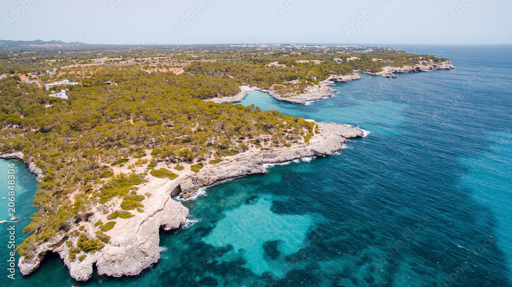 Aerial drone view of beautiful turquoise sea with rocky shore and green trees. Island of Mallorca, Spain. Sunny summer day