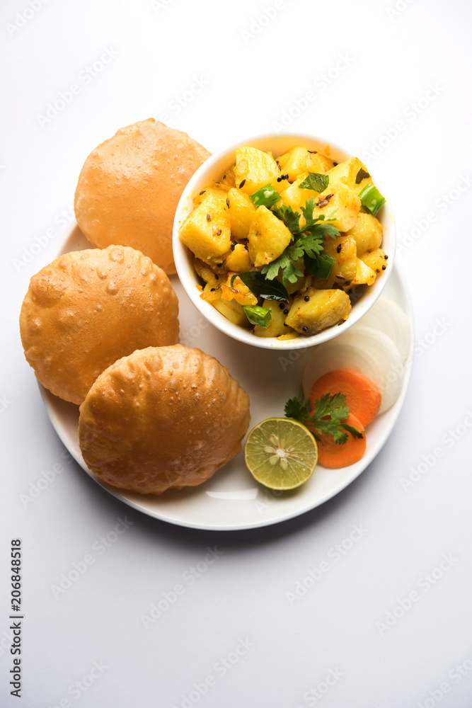Chatpate Masala Aloo Sabzi fry OR Bombay potatoes served with fried puri or Indian bread made up of wheat in a plate, selective focus Chatpate Masala Aloo Sabzi fry OR Bombay potatoes served with fried puri or Indian bread made up of wheat in a plate, selective focus