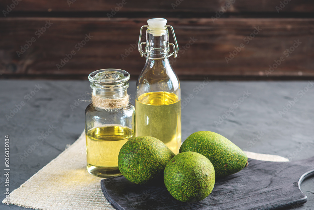 Avocado fruit and oil in glass bottle on dark background. Concept organic eco products for food and cosmetic procedures Avocado fruit and oil in glass bottle on dark background. Concept organic eco products for food and cosmetic procedures