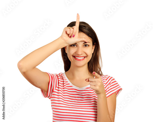 Obraz na plátně a happy woman gives a sign of the loser on his forehead, looking at you and pointing his finger at the camera