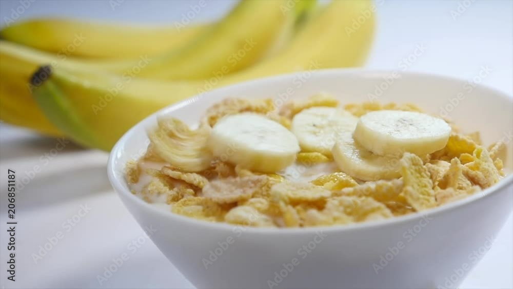 Corn flakes with milk are in a bowl. pieces of banana fall on the top of this delicious breakfast. Close-up shot Corn flakes with milk are in a bowl. pieces of banana fall on the top of this delicious breakfast. Close-up shot