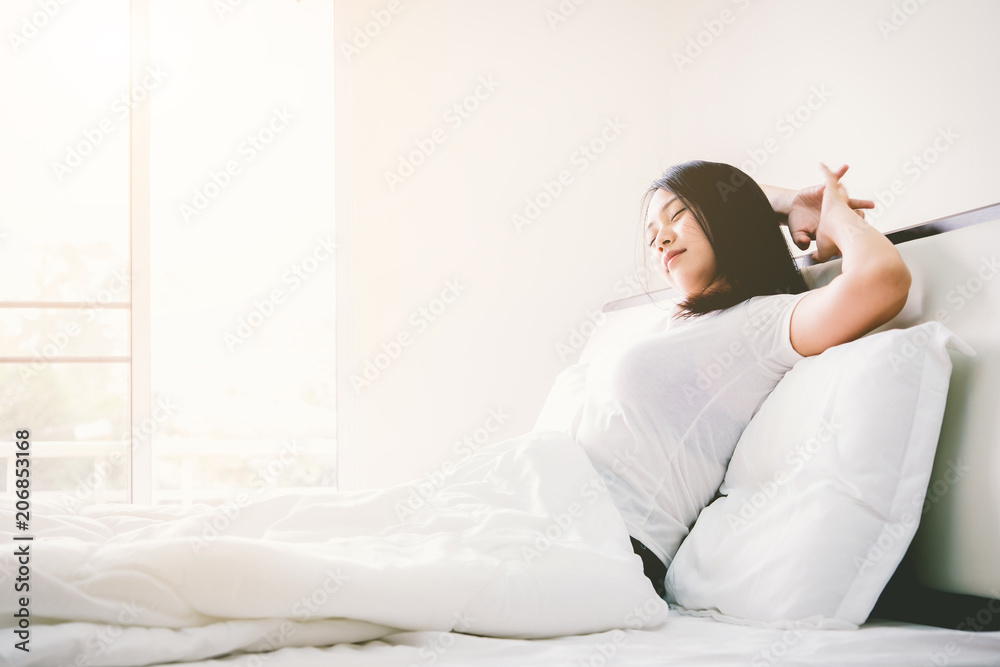 Young asian beautiful woman waking up in her bed fully rested. Woman stretching in bed after wake up. Healthy lifestyle. Wellness concept