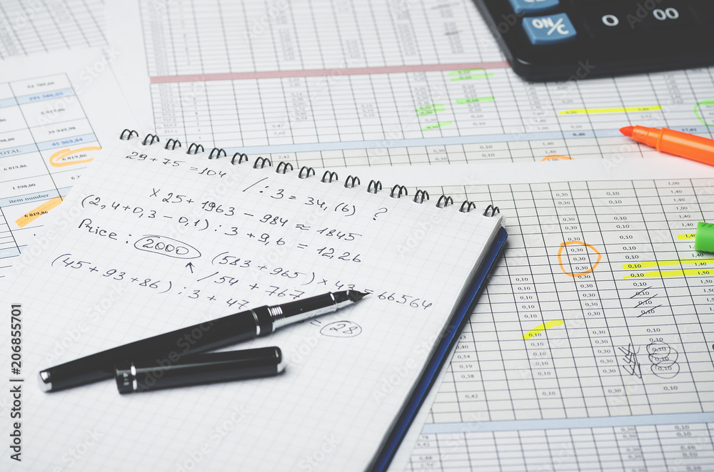 Paper notebook with accounting calculations and pen on the background of a table with numbers Paper notebook with accounting calculations and pen on the background of a table with numbers