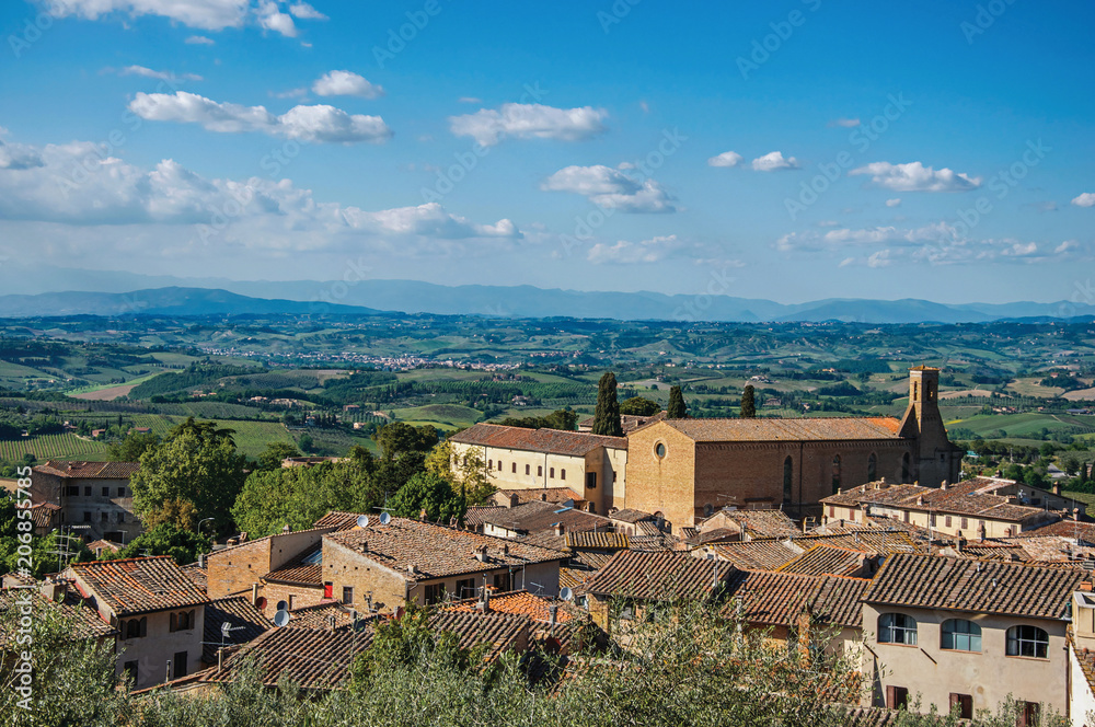Overview of rooftops and church with green hills and blue sky at San Gimignano. An amazing medieval town famous for having several towers in its historical center. Located in the Tuscany region 