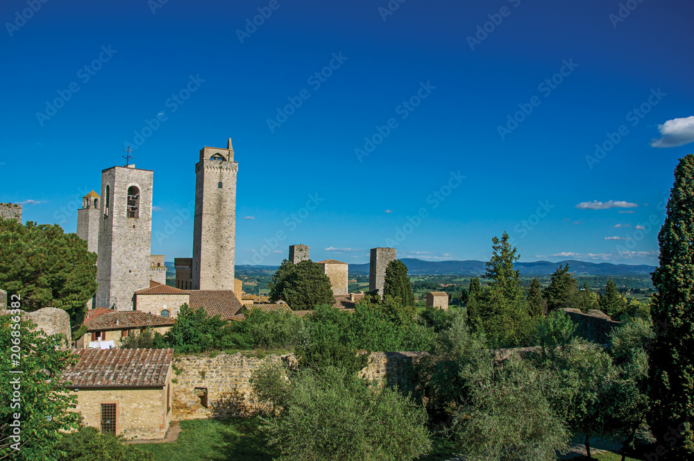 View of rooftops and towers with trees and blue sunny sky at San Gimignano. An amazing medieval town famous for having several towers in its historical center. Located in the Tuscany region 