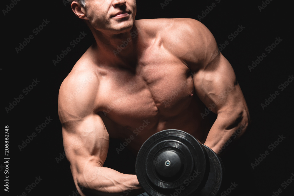 Handsome power athletic man with dumbbell confidently looking forward. Strong bodybuilder with six pack, perfect abs, shoulders, biceps, triceps and chest. Strength and motivation
