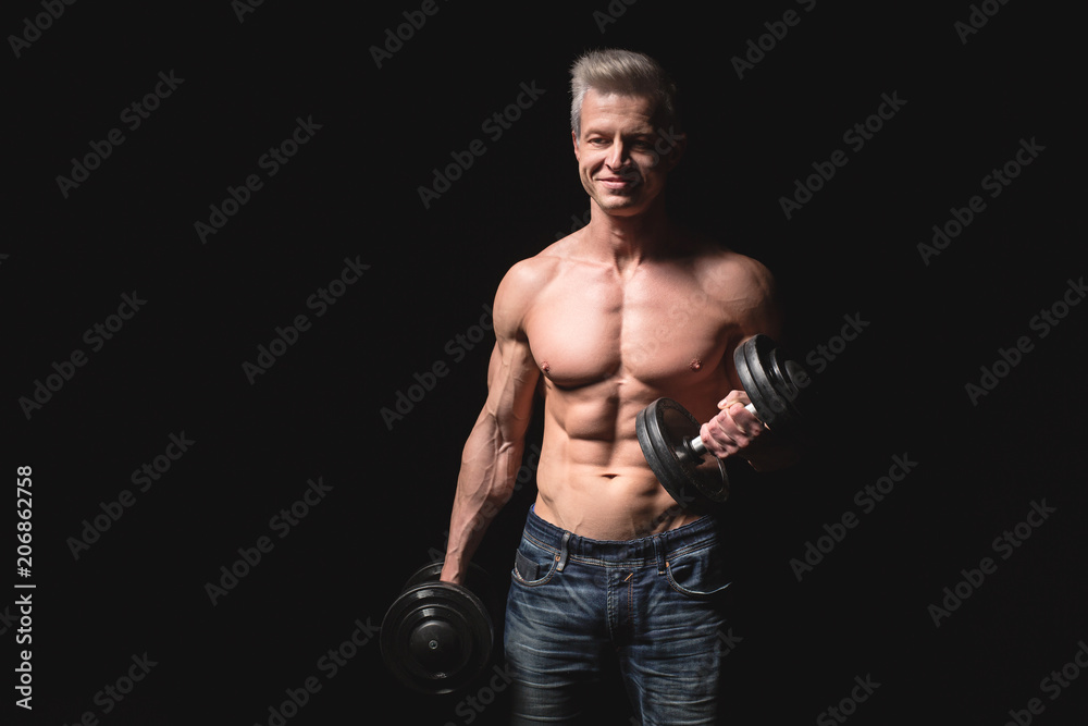 Handsome power athletic man with dumbbell confidently looking forward. Strong bodybuilder with six pack, perfect abs, shoulders, biceps, triceps and chest. Strength and motivation