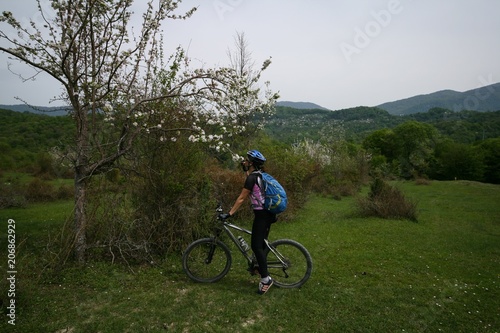 Young woman riding a bike near a flowering tree in the mountains