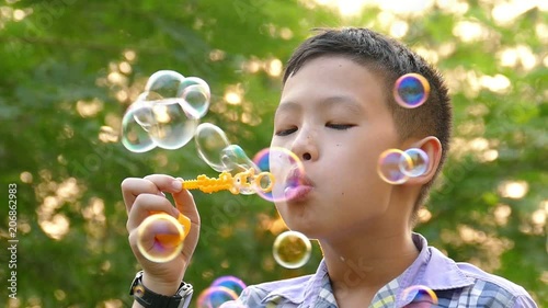 Young asian boy blowing soap bubbles in park ,slow motion.
