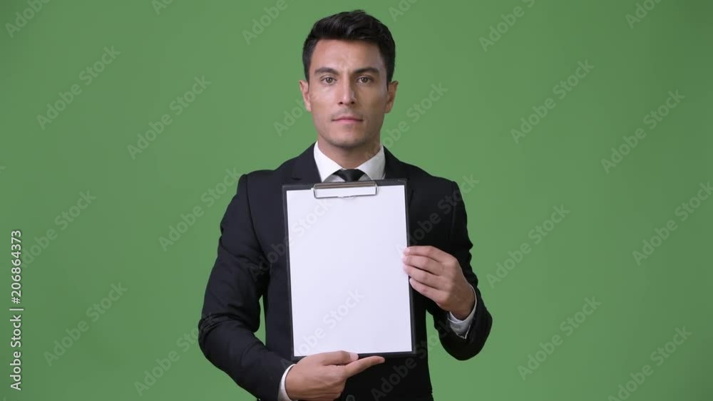 Young handsome Hispanic businessman against green background