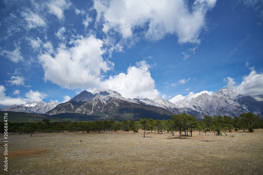 Landscape view of Jade Dragon Snow Mountain with blue sky and trees in bottom of mountain. It`s famous place in China for travel. Landscape view of Jade Dragon Snow Mountain with blue sky and trees in bottom of mountain. It`s famous place in China for travel.