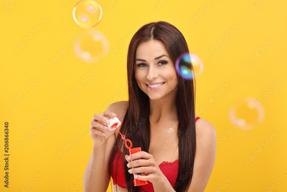 Woman with bubbles against yellow wall background Woman with bubbles against yellow wall background
