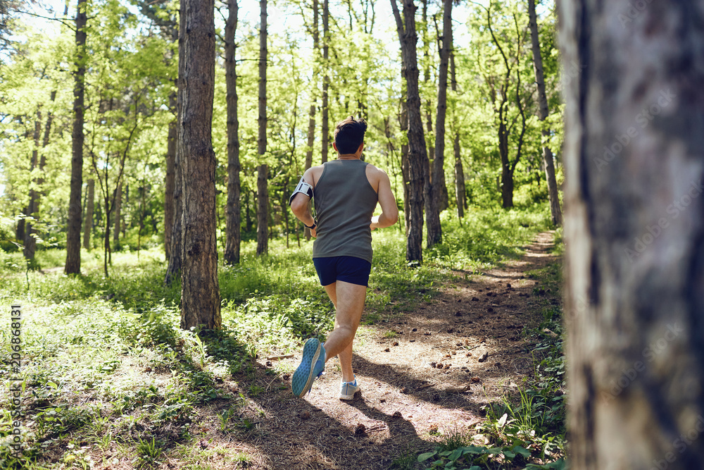 A young male runner runs in the forest in the summer.