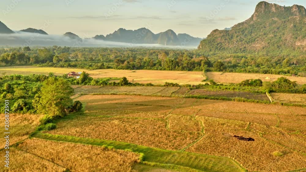 Aerial rural mountain valley sunrise view. Aerial bird's-eye sunrise time view on valley landscape with karst mountains and rice fields. Laos, Vang Vieng.